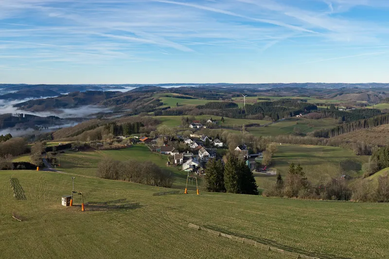 Wildewiese w górach Sauerlandu, z wyciągiem narciarskim na łące i wioską u jej podnóża
